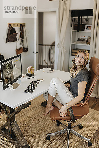 Lächelnde Frau sitzt auf einem Stuhl und arbeitet zu Hause