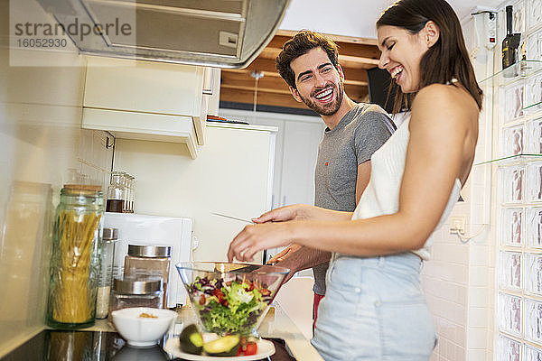 Fröhliches junges Paar bei der Zubereitung einer gemeinsamen Mahlzeit in der Küche zu Hause