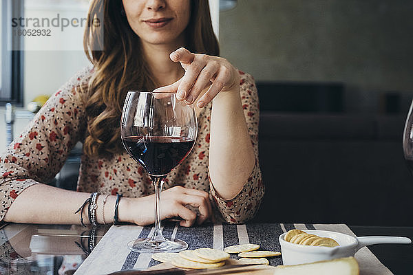 Junge Frau berührt ein Weinglas  während sie am Esstisch sitzt