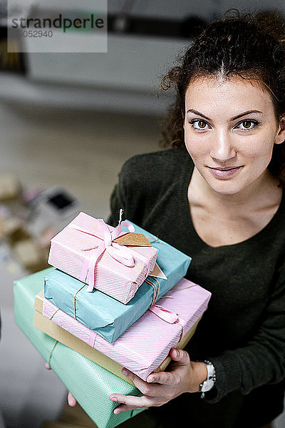 Porträt einer lächelnden jungen Frau mit einem Stapel eingepackter Geschenke