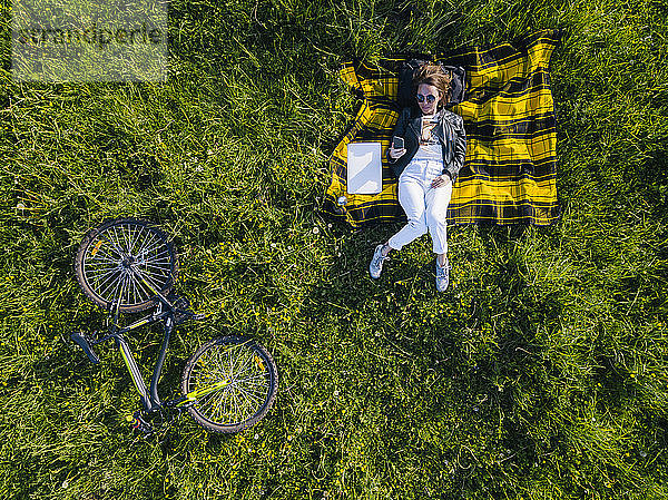 Frau mit Smartphone im Gras liegend  Luftaufnahme