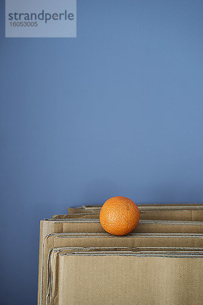 Einzelne Orange auf Karton gegen blaue Wand