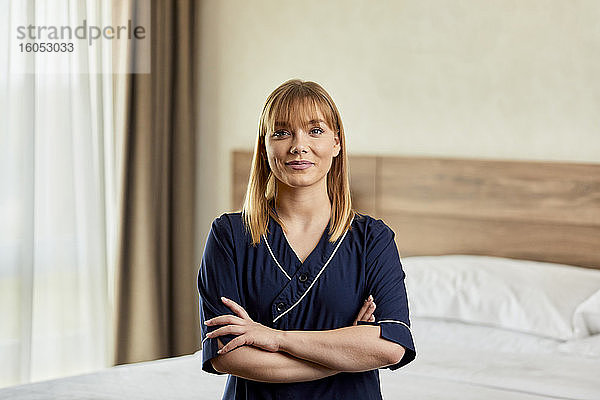 Selbstbewusstes Zimmermädchen mit verschränkten Armen im Schlafzimmer eines Hotels