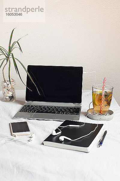 Mobiltelefon mit Buch und Tee am Laptop auf dem Schreibtisch an der Wand im Büro