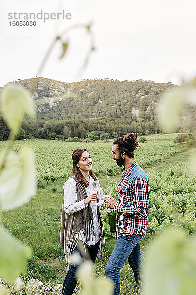 Glückliches Paar mit Weingläsern in der Hand im Gespräch auf einem Weinberg