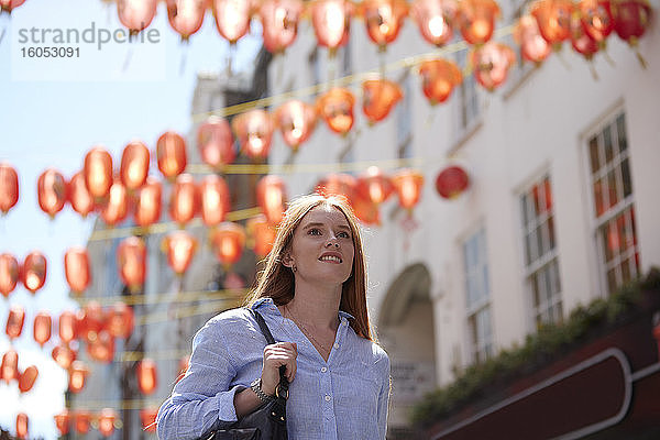 Nachdenkliche junge Frau geht unter chinesischen Laternen in der Stadt spazieren
