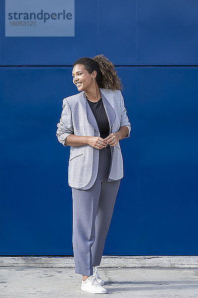 Lächelnde Geschäftsfrau vor einer blauen Wand