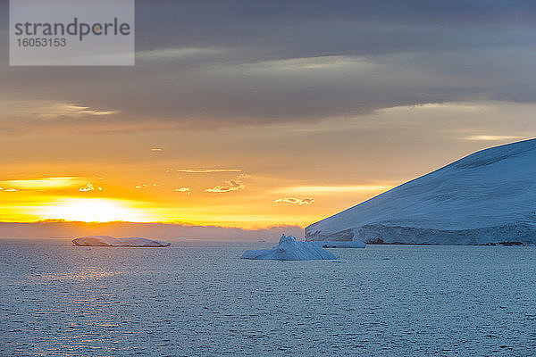 Antarktische Küstenlinie bei bewölktem Sonnenuntergang