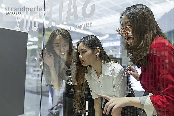 Neugierige Freundinnen beim Schaufensterbummel durch Glas im Einkaufszentrum gesehen
