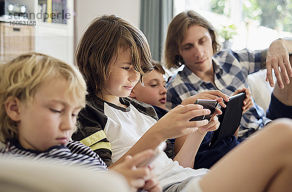 Vater schaut auf Jungen  die im Wohnzimmer Spiele auf Smartphones und digitalen Tabletts spielen