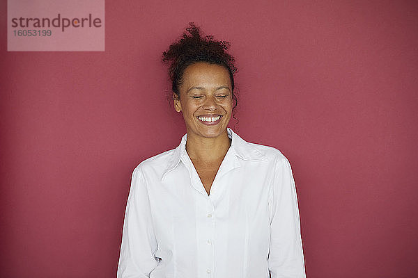 Porträt einer lächelnden Geschäftsfrau mit geschlossenen Augen vor rotem Hintergrund