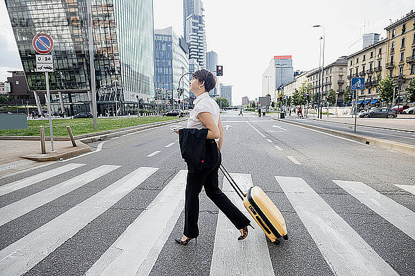 Unternehmerin mit Koffer beim Überqueren der Straße in der Stadt