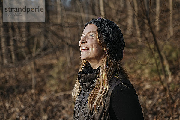Lächelnde Frau im mittleren Erwachsenenalter  die im Wald stehend nach oben schaut