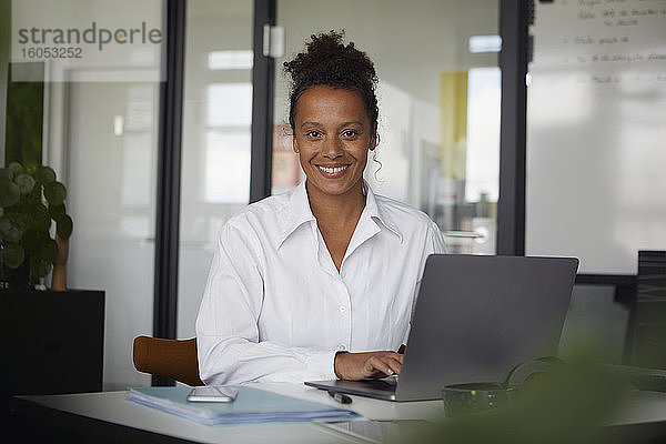 Porträt einer lächelnden Geschäftsfrau  die im Büro am Laptop arbeitet