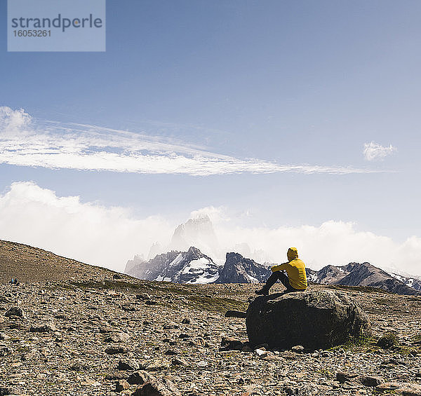 Männlicher Wanderer  der auf einem Felsen sitzend die Landschaft gegen den Himmel betrachtet  Patagonien  Argentinien