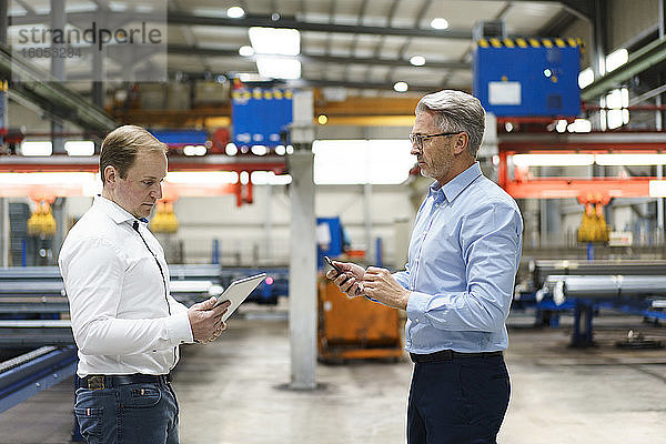 Zwei Geschäftsleute mit Tablet und Mobiltelefon bei einem Treffen in einer Fabrik
