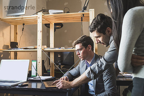 Drei Geschäftsleute teilen sich einen Laptop am Schreibtisch im Büro