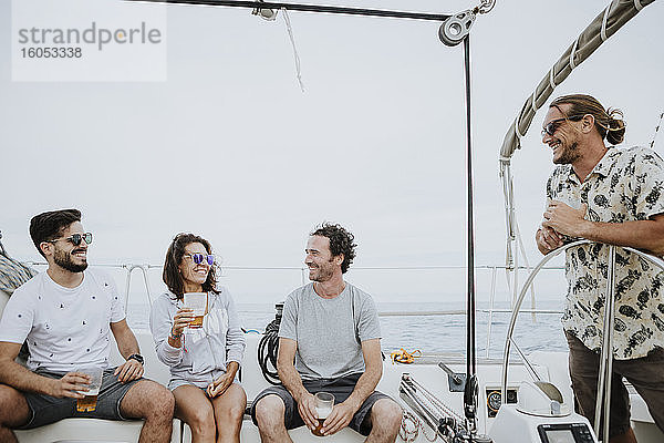 Fröhliche Freunde haben Spaß und genießen Bier auf einem Segelboot gegen den klaren Himmel
