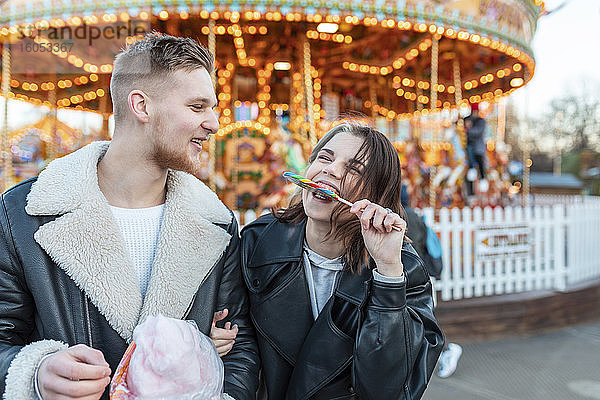 Glücklicher Mann  der seine Freundin ansieht  die im Vergnügungspark einen Lutscher isst