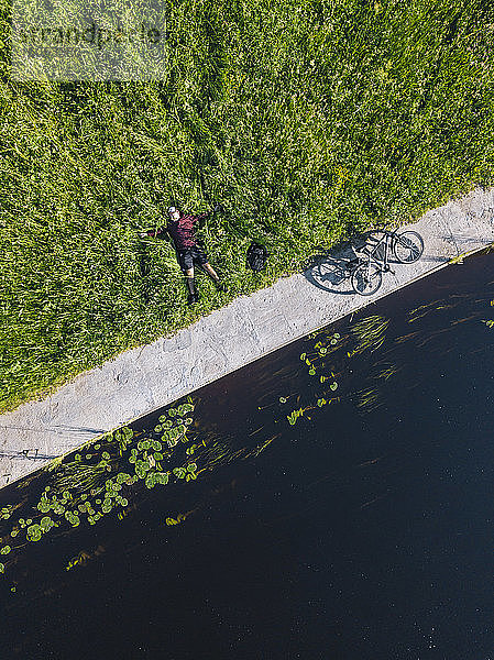 Luftaufnahme eines mittleren erwachsenen Mannes mit Fahrrad auf einer Wiese am Flussufer