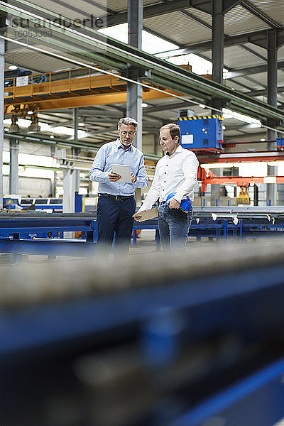 Zwei Geschäftsleute mit Tablet im Gespräch in einer Fabrik