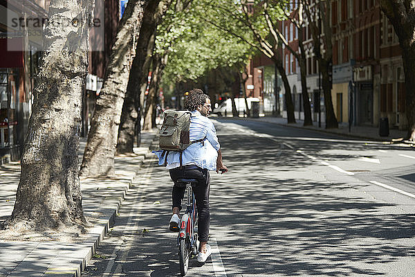 Rückansicht eines jungen Mannes  der mit einem Leihfahrrad auf einem Fahrradweg fährt  London  UK