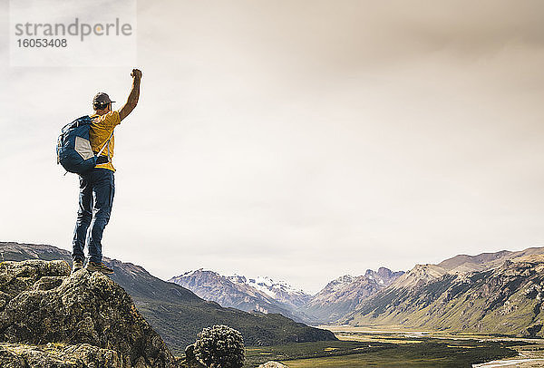Mann mit erhobenem Arm  der auf einem Felsen stehend die Berge betrachtet  Patagonien  Argentinien