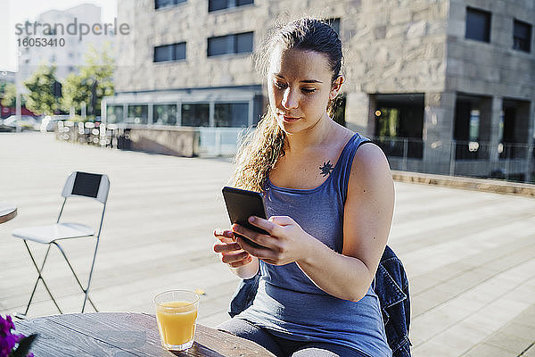 Sportliche junge Frau  die ihr Smartphone benutzt  während sie in einem Straßencafé in der Stadt sitzt