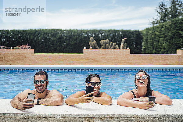 Lachende Freunde bei einer Poolparty mit Smartphones
