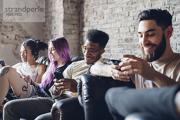 Gruppe von Freunden sitzt auf dem Sofa in einem Loft und benutzt Smartphones