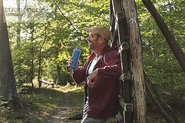 Lächelnder reifer Mann  der eine Wasserflasche hält  während er an einer Holzleiter im Park steht