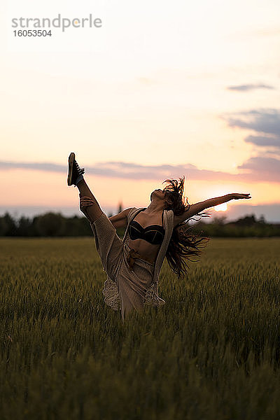 Frau tanzt bei Sonnenuntergang auf einem Feld