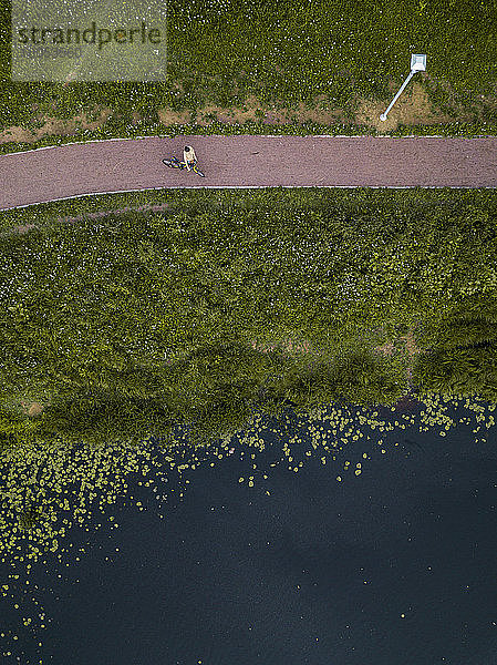 Russland  Tichwin  Luftaufnahme einer Radfahrerin  die auf einem Fußweg am Seeufer im Park eine Pause einlegt