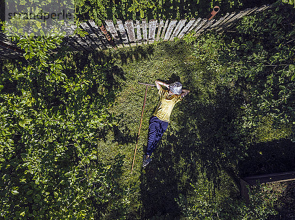 Luftaufnahme einer mittleren erwachsenen Frau mit den Händen hinter dem Kopf  die auf einer Wiese im Hof ruht