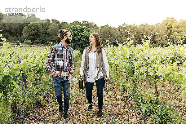 Glückliches Paar mit Weingläsern und Weinflasche beim Spaziergang im Weinberg