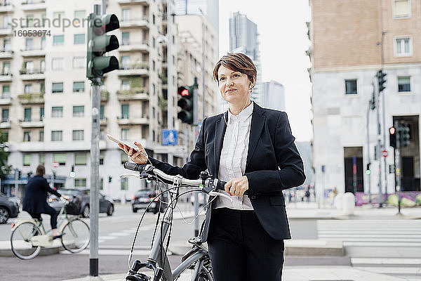 Weibliche Fachkraft hört Musik  während sie mit dem Fahrrad auf einer Straße in der Stadt spazieren geht