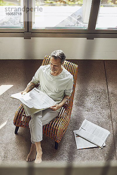 Älterer Mann sitzt auf einem Stuhl in einer Dachgeschosswohnung und liest Zeitung