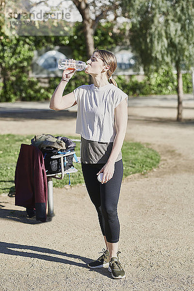 Frau trinkt Wasser während eines Workouts im Park
