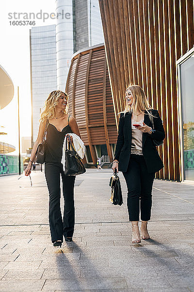 Weibliche Kollegen unterhalten sich beim Gehen auf dem Bürgersteig in der Stadt