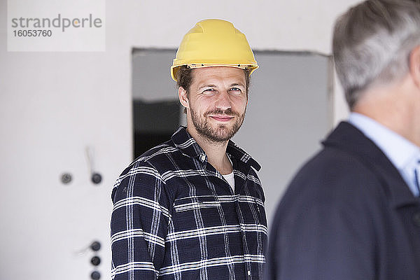 Ein lächelnder Bauarbeiter steht mit einem Architekten beim Bau eines Hauses.