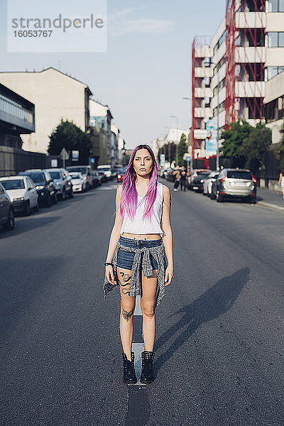 Porträt einer stilvollen jungen Frau mit rosa Haaren auf der Straße in der Stadt stehend