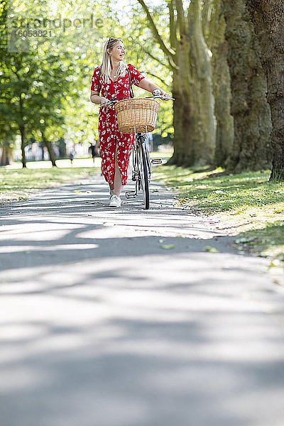 Frau schaut weg  während sie mit dem Fahrrad auf dem Fußweg in einem öffentlichen Park an einem sonnigen Tag spazieren geht