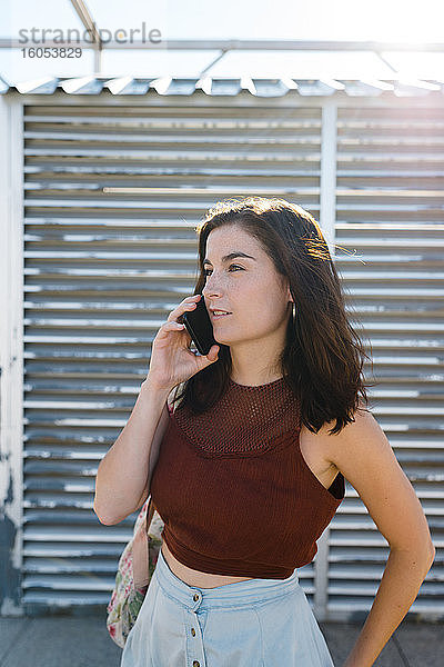 Schöne Frau  die ein Smartphone benutzt  während sie an einem sonnigen Tag vor einem Fensterladen steht