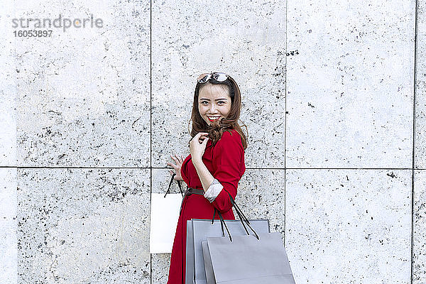 Lächelnde Frau  die Einkaufstüten trägt  während sie an der Wand steht