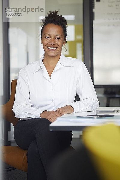Porträt einer lächelnden Geschäftsfrau  die am Schreibtisch im Büro sitzt