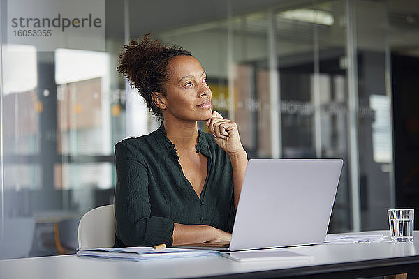 Porträt einer nachdenklichen Geschäftsfrau  die mit einem Laptop am Schreibtisch sitzt und in die Ferne schaut