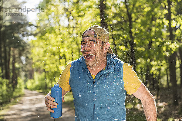 Fröhlicher Mann schaut weg  während er inmitten von Wassertropfen im Park steht