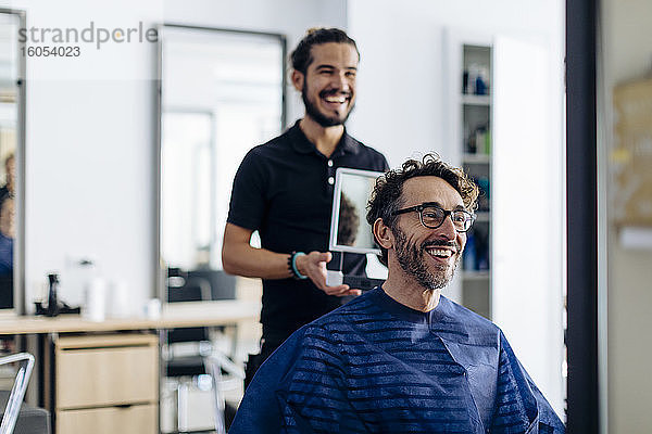 Glückliche Friseurin zeigt dem Kunden im Spiegel den Haarschnitt im Salon