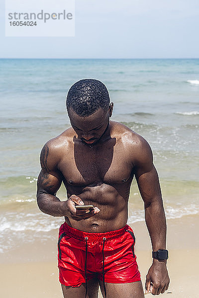 Sportlicher Mann mit Smartphone am Strand