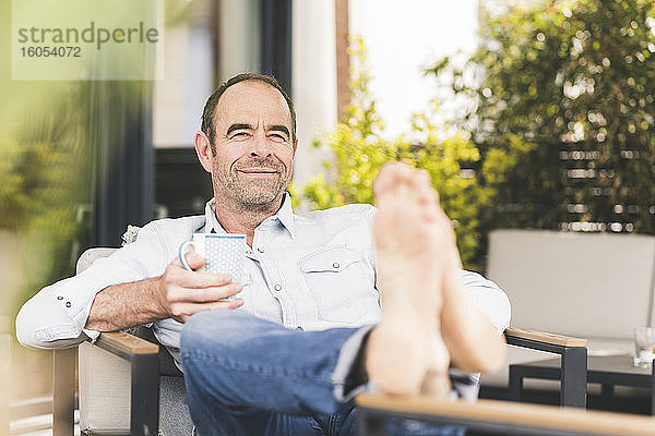 Lächelnder Mann sitzt mit Kaffeetasse im Hinterhof